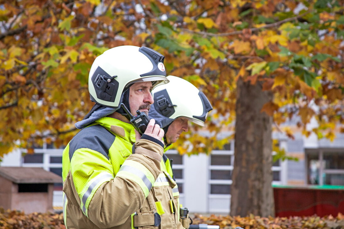 Feuerwehrleute im Einsatz. Ein Feuerwehrmann spricht in ein Handfunkgerät.